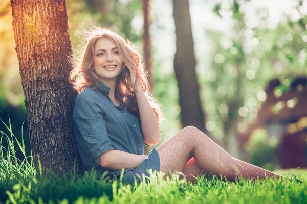 Jolie jeune femme caucasienne assise dehors sous un arbre parlant sur un appareil smartphone. Effets filtrés — Photo