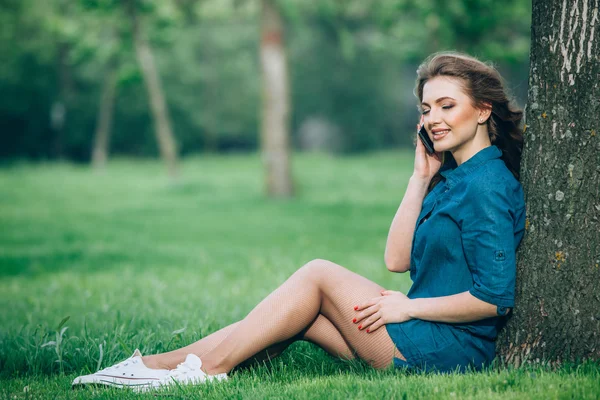 Jolie jeune femme caucasienne assise dehors sous un arbre parlant sur un appareil smartphone. Effets filtrés — Photo