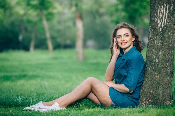 Hübsche junge kaukasische Frau, die draußen unter einem Baum sitzt und mit einem Smartphone spricht. Gefilterte Effekte — Stockfoto