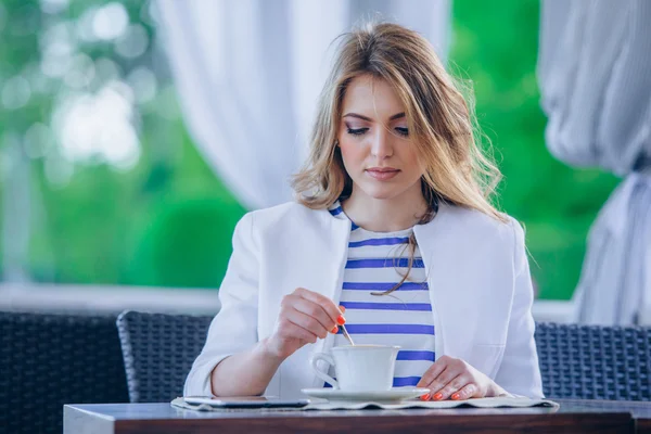 Hermosa joven en la cafetería al aire libre leyendo un libro y beber café. teléfono. Estudiante. mujer de negocios — Foto de Stock