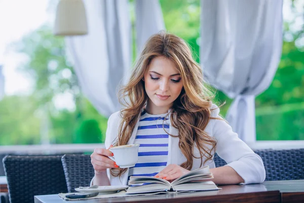 Hermosa joven en la cafetería al aire libre leyendo un libro y beber café. teléfono. Estudiante. mujer de negocios — Foto de Stock