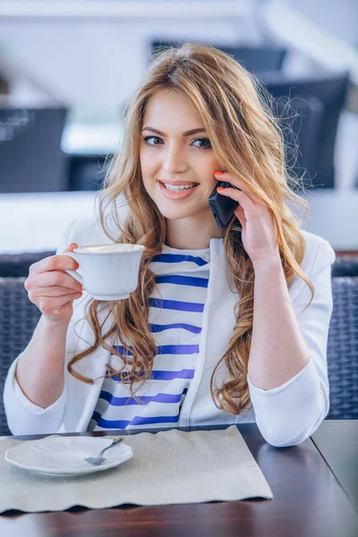 Mujer joven en la cafetería bebe café y habla por teléfono móvil — Foto de Stock