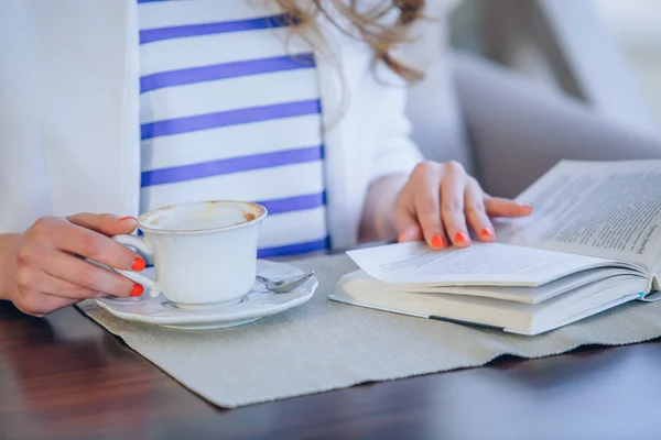 beautiful young girl in outdoor cafe reading a book and drinking coffee. phone. student. business woman