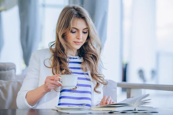 Hermosa joven en la cafetería al aire libre leyendo un libro y beber café. teléfono. Estudiante. mujer de negocios — Foto de Stock