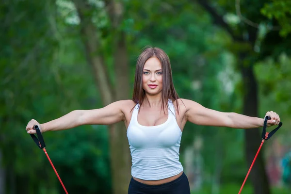 Fitness, sport, koncepcja ludzie i styl życia - uśmiechnięta kobieta robi ćwiczenia z expander w plenerze, park — Zdjęcie stockowe