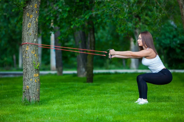 Fitness, sport, lidé a životní styl koncept - usmívající se žena dělá cvičení s expandér v přírodě, park — Stock fotografie