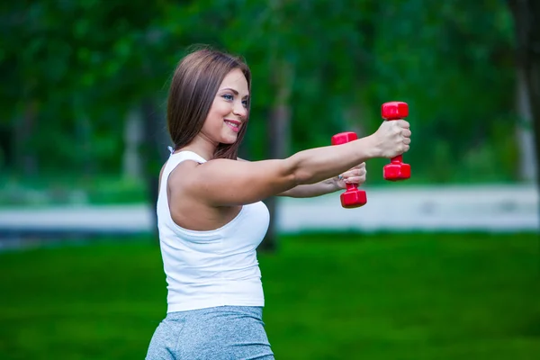 Mulher trabalhando com pequenos halteres no parque, de manhã . — Fotografia de Stock