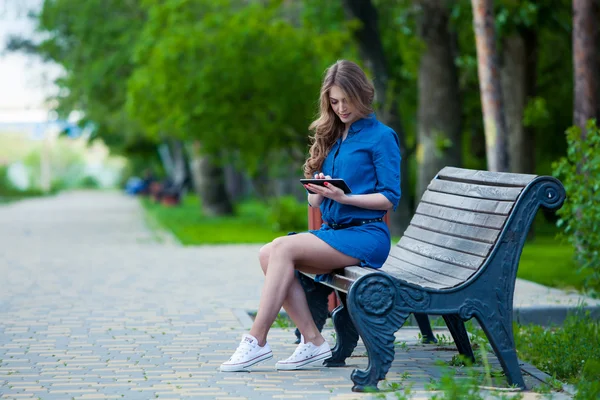 Seitenansicht einer jungen Frau mit Tablet-Computer auf Parkbank — Stockfoto