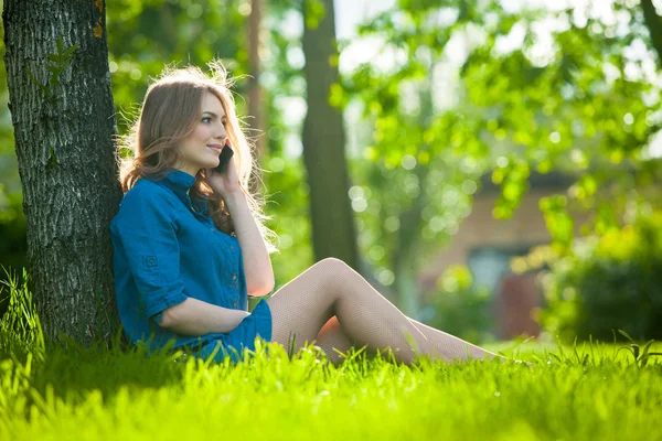 Jolie jeune femme caucasienne assise dehors sous un arbre parlant sur un appareil smartphone. Effets filtrés — Photo