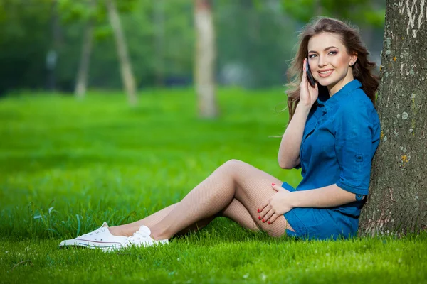 Jolie jeune femme caucasienne assise dehors sous un arbre parlant sur un appareil smartphone. Effets filtrés — Photo