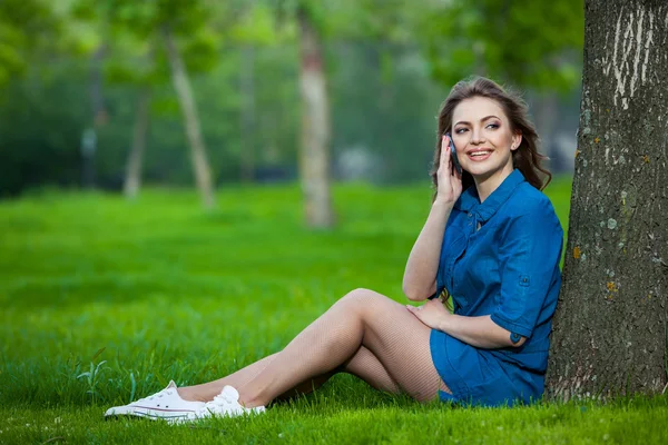 Pretty young caucasian woman  sitting outside under a tree talking on smartphone device. Filtered effects — Stock Photo, Image