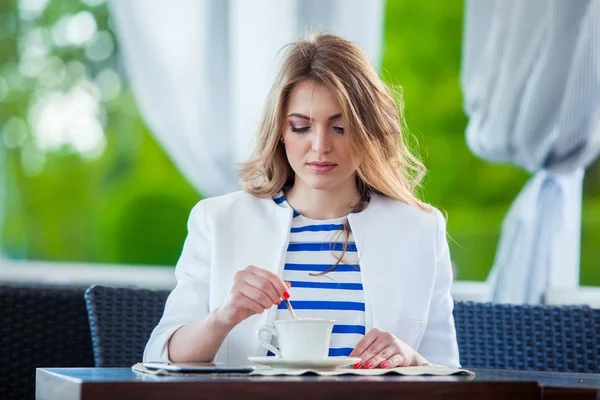 Hermosa joven en la cafetería al aire libre leyendo un libro y beber café. teléfono. Estudiante. mujer de negocios — Foto de Stock