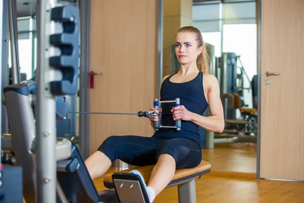 Sport, fitness, livsstil och människor koncept - ung kvinna flexar muskler på gymmet maskin — Stockfoto