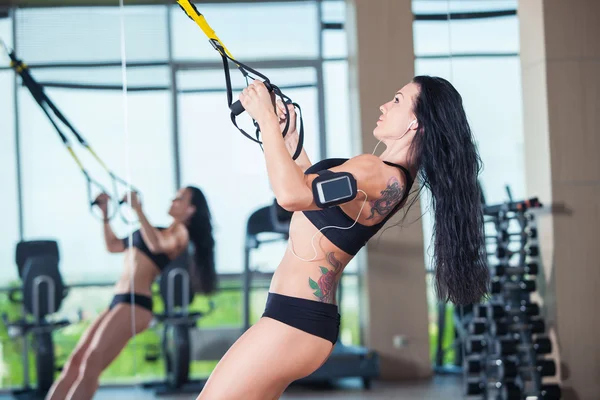 Atractiva mujer hace crossfit flexiones con correas de fitness trx en el estudio de gimnasios — Foto de Stock