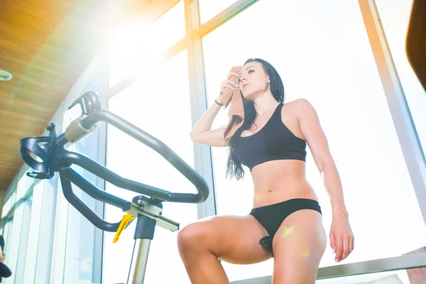 Beautiful woman at the gym on bike, cycle, sunny gym, general plan, weary — Stock Photo, Image