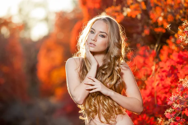 Junge Frau auf einem Hintergrund aus roten und gelben Herbstblättern mit schönen lockigen Haaren auf der Brust, keine Kleidung — Stockfoto