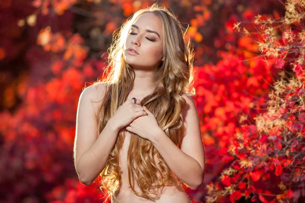 Junge Frau auf einem Hintergrund aus roten und gelben Herbstblättern mit schönen lockigen Haaren auf der Brust, keine Kleidung — Stockfoto