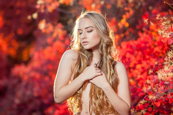 赤と黄色の秋の背景に若い女性は彼の胸、服美しい巻き毛を持つ葉します。 — ストック写真