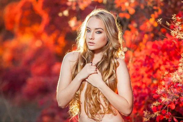 Junge Frau auf einem Hintergrund aus roten und gelben Herbstblättern mit schönen lockigen Haaren auf der Brust, keine Kleidung — Stockfoto