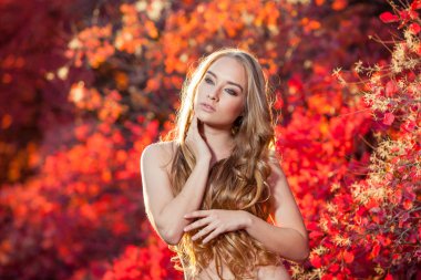 Kırmızı ve sarı sonbahar bir arka plan üzerinde genç kadın güzel kıvırcık saçlı göğsüne çıplak bırakır.