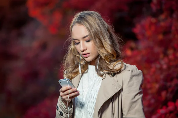 Unga skönhet kvinna skriva meddelande på mobilen i en höst park — Stockfoto