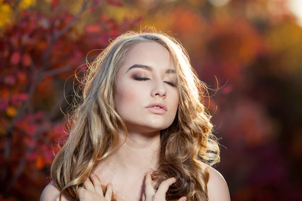 Hermosa joven con el pelo rizado sobre un fondo de hojas de otoño rojas y amarillas — Foto de Stock