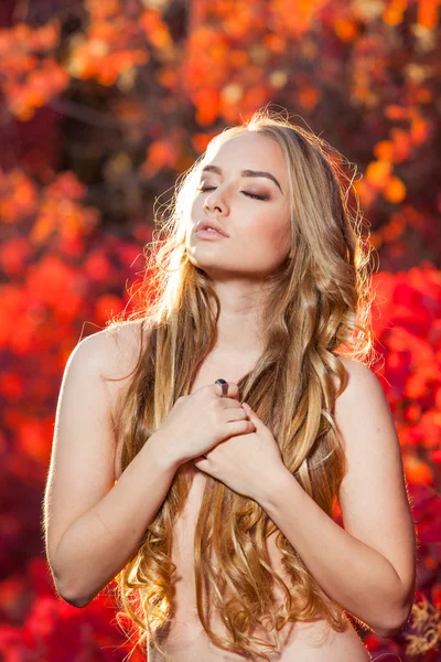 Jeune femme sur un fond de feuilles d'automne rouges et jaunes avec de beaux cheveux bouclés sa poitrine, sans vêtements — Photo