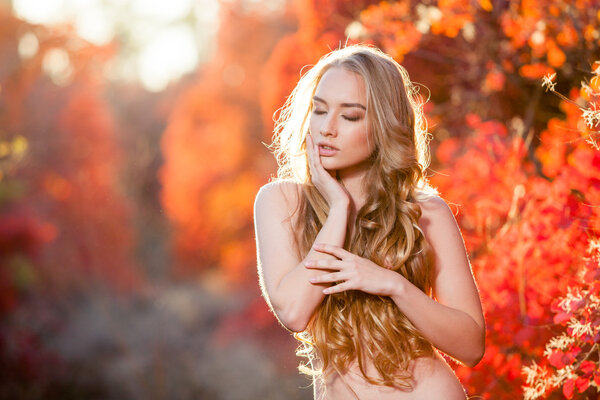 young woman on a background of red and yellow autumn leaves with beautiful curly hair his chest, no clothes