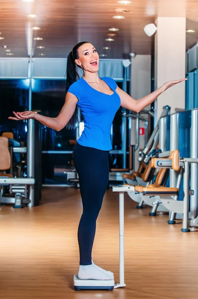 Lycklig kvinna ler på vågar på gym — Stockfoto