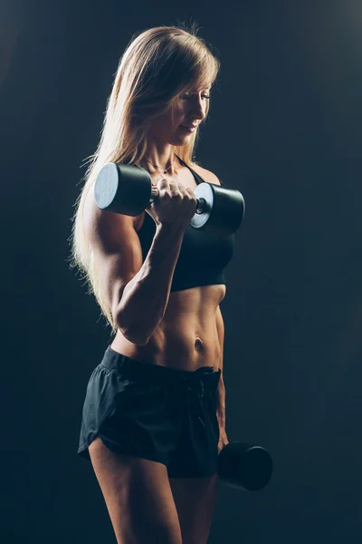 Mulher atlética com halteres em um fundo escuro — Fotografia de Stock