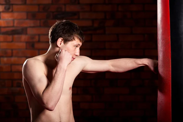 muscular handsome fighter giving a forceful forward kick during  practise round with  boxing bag, kickboxing