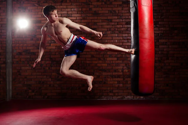 Muscular handsome fighter giving a forceful forward kick during  practise round with  boxing bag, kickboxing — Stock Photo, Image