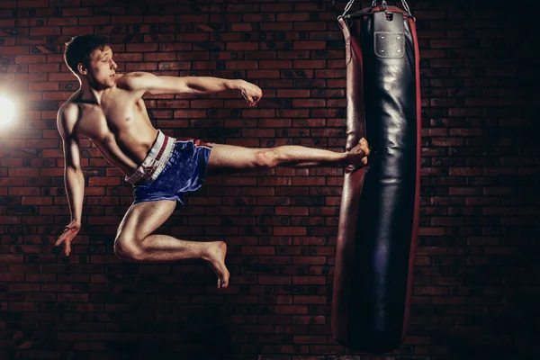 Musculoso guapo luchador dando una fuerte patada hacia adelante durante la ronda de práctica con bolsa de boxeo, kickboxing —  Fotos de Stock
