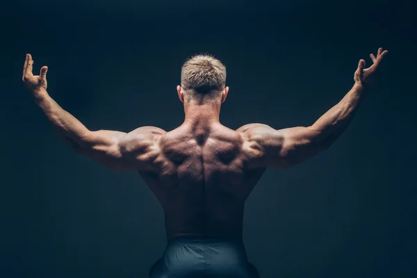 Schöner muskulöser Bodybuilder posiert vor schwarzem Hintergrund. — Stockfoto