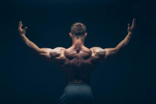 Schöner muskulöser Bodybuilder posiert vor schwarzem Hintergrund. — Stockfoto