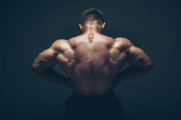 Schöner muskulöser Bodybuilder posiert vor schwarzem Hintergrund. — Stockfoto