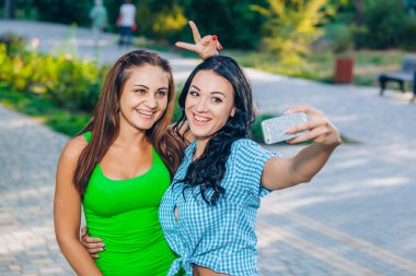 two beautiful young women using smart phone for selfie in the park