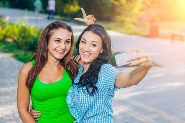 two beautiful young women using smart phone for selfie in the park