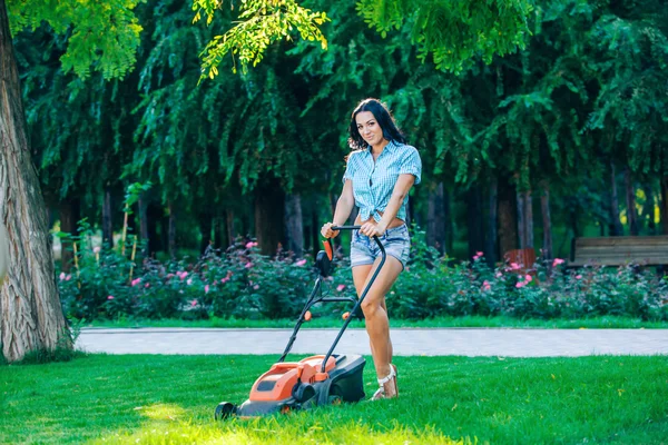 Woman mowing lawn in residential back garden on sunny day — Stockfoto