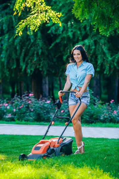 Femme tondre la pelouse dans le jardin résidentiel arrière par une journée ensoleillée — Photo