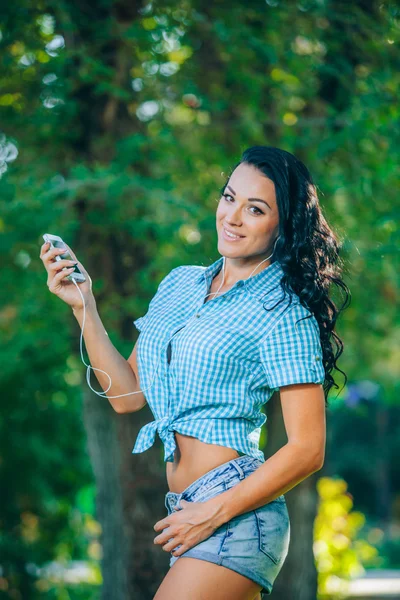 Young hipster stylish beautiful girl listening to music, mobile phone,headphones, enjoying, denim outfit, smiling, happy, cool accessories, having fun, laughing, park — Φωτογραφία Αρχείου