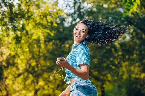 Jovem hipster elegante menina bonita ouvir música, telefone celular, fones de ouvido, desfrutando, roupa jeans, sorrindo, feliz, acessórios legais, se divertindo, rindo, parque — Fotografia de Stock