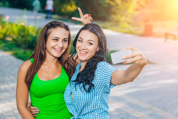 Two beautiful young women using smart phone for selfie in the park — Stok fotoğraf