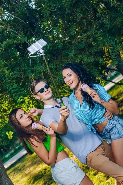 Grupo de amigos tirando foto-se com monopod usar telefone inteligente tirar foto selfie stick no parque — Fotografia de Stock