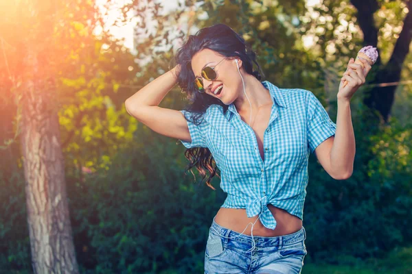 Young beautiful short blue hair hipster woman with headphones music in the park. ice cream — ストック写真