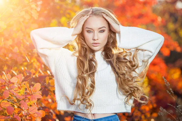 Schöne junge Frau mit lockigem Haar vor einem Hintergrund aus roten und gelben Herbstblättern — Stockfoto