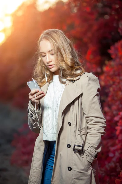 Junge Schönheit schreibt Nachricht auf Handy in einem herbstlichen Park — Stockfoto