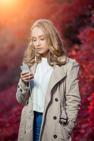 Schoonheid van de jonge vrouw schriftelijk bericht op mobiele telefoon in een herfst park — Stockfoto