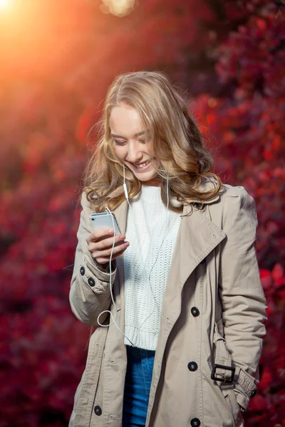 Schoonheid van de jonge vrouw schriftelijk bericht op mobiele telefoon in een herfst park — Stockfoto