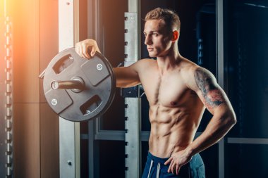 Closeup portrait of a muscular man workout with barbell at gym. Brutal bodybuilder athletic six pack, perfect abs, shoulders, biceps, triceps and chest